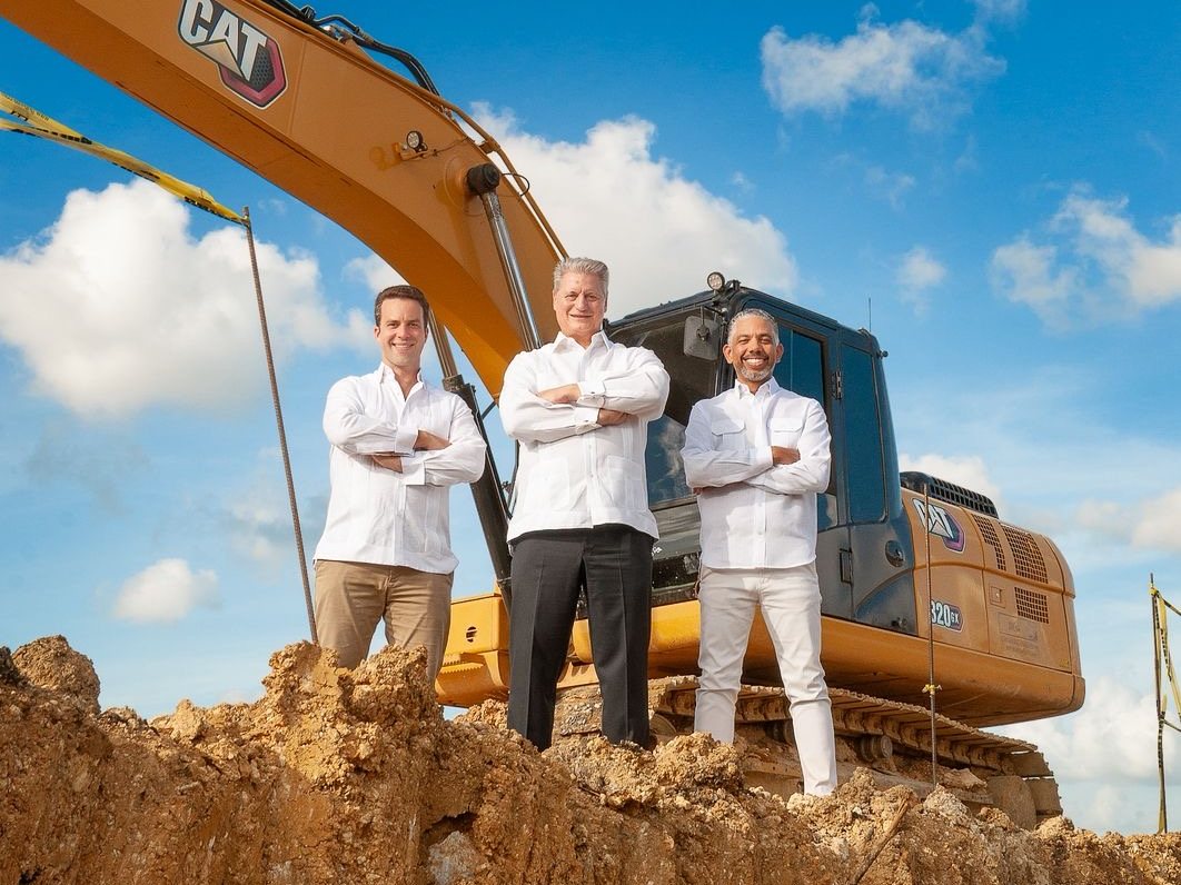 Los tres socios de Riverside sobre el terreno excavado, frente a la excavadora, el día del lanzamiento.